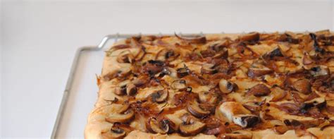 Focaccia recién horneada, dorada y cubierta con cebolla caramelizada y otros toppings