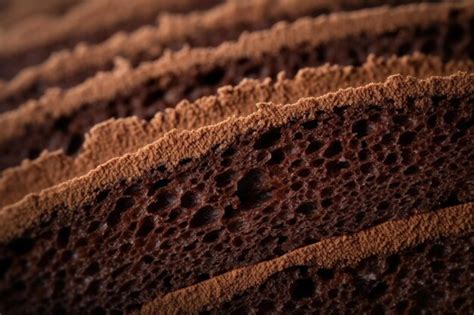 Fotografía profesional de un bizcocho de chocolate keto con textura húmeda y un glaseado brillante, decorado con frambuesas frescas.