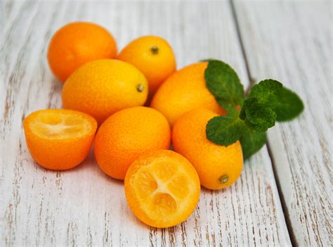 Fotografía detallada de frutos de kumquat frescos y brillantes sobre una mesa de madera rústica.