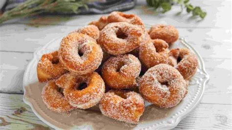 Fotografía cenital de rosquillas recién fritas y rebozadas en azúcar sobre una bandeja de madera