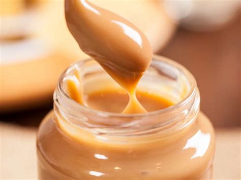 Foto de primer plano de dulce de leche en un recipiente de vidrio, con un postre de fondo