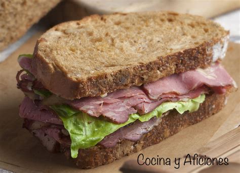 Sándwich de pastrami recién preparado con pan negro y pepinillos.