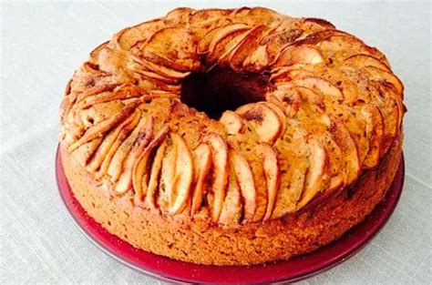 Foto profesional de un queque de manzana recién horneado, con láminas de fruta y una ligera capa de azúcar flor sobre una mesa de madera.
