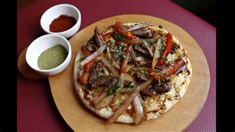 Fotografía gastronómica de una pizza de lomo saltado recién horneada con los ingredientes característicos del plato peruano.