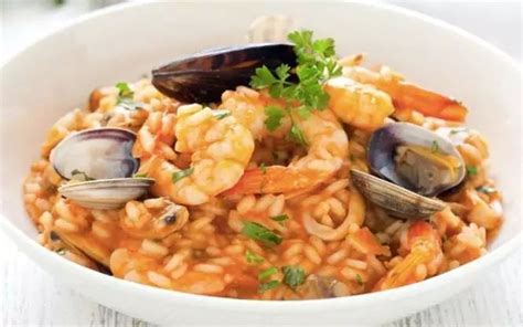 Primer plano de un plato de risotto de mariscos con salsa de tomate, adornado con camarones.