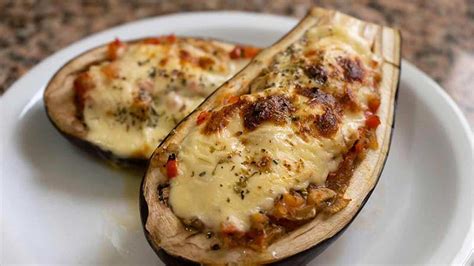 Imagen de berenjenas rellenas recién salidas del horno con una capa dorada de queso fundido y toques de perejil.