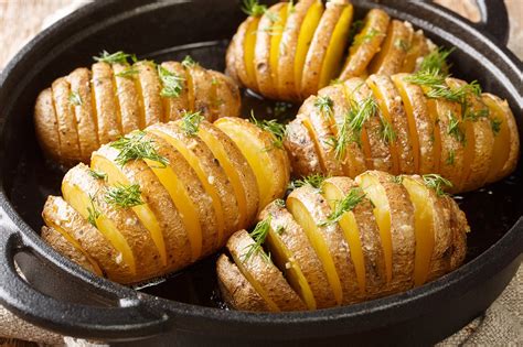 Patatas Hasselback crudas con los cortes característicos y untadas con mantequilla y romero.