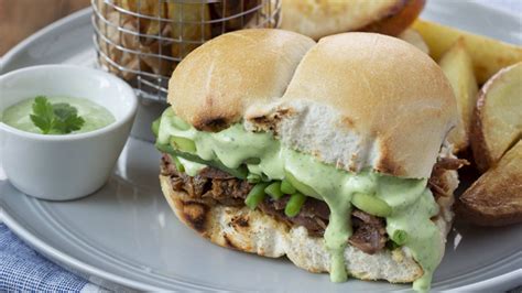 Ilustración de un sandwich de marraqueta abierto, mostrando las capas de carne mechada, tomate, palta y mayonesa, junto a una porción de papas fritas doradas.