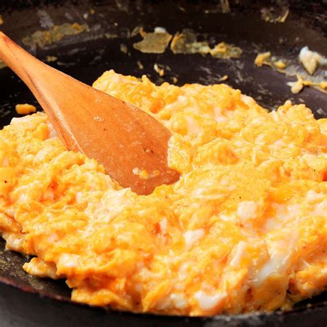 Esquema de pasos para cocinar huevos revueltos: batido, cocción a fuego lento y emplatado final