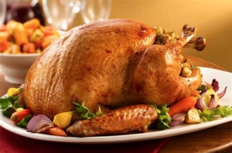 Fotografía de una gallina horneada dorada rodeada de vegetales frescos lista para servir en una mesa familiar.