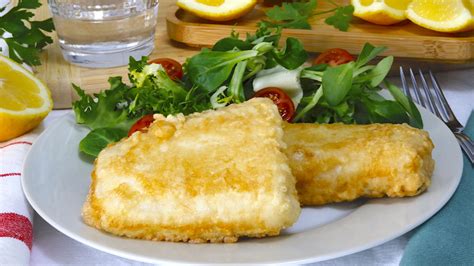 Plato de filetes de merluza a la romana recién fritos, servidos con rodajas de limón y una guarnición de ensalada fresca.