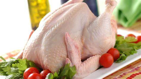 Imagen de un pollo crudo siendo preparado con hierbas y limón antes de asar