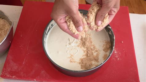Fotografía cenital de una base de galleta triturada con mantequilla lista para hornear en un molde desmontable.