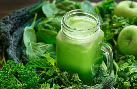 Fotografía gastronómica de un jugo verde fresco en un vaso de cristal con ingredientes naturales alrededor.