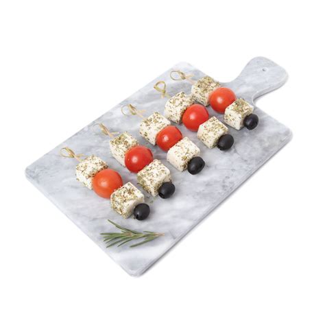 Plato elegante con brochetas de queso de cabra, aceitunas verdes y tomates cherry decorado con hojas frescas de albahaca.