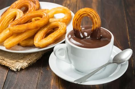 Fotografía de churros recién hechos con un cuenco de chocolate caliente al lado, espolvoreados con azúcar y canela.