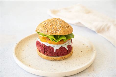 Plato servido de hamburguesa de remolacha y lentejas con pan integral y vegetales frescos