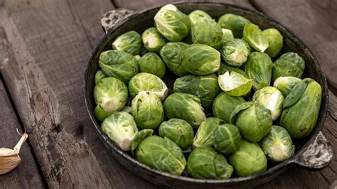 Plato de repollitos de Bruselas frescos presentados junto a especias y aceite de oliva para su preparación.