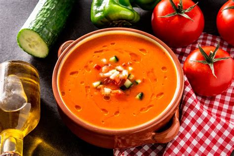 Foto cenital de un cuenco de gazpacho de pepino decorado con albahaca fresca y un chorrito de aceite de oliva sobre una mesa de madera veraniega.