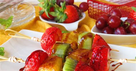 Fotografía de una selección de frutas caramelizadas y postres diversos preparados sobre una parrilla con brasas vivas.