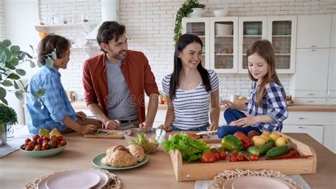 Padres e hijos sonriendo mientras preparan juntos una ensalada colorida.