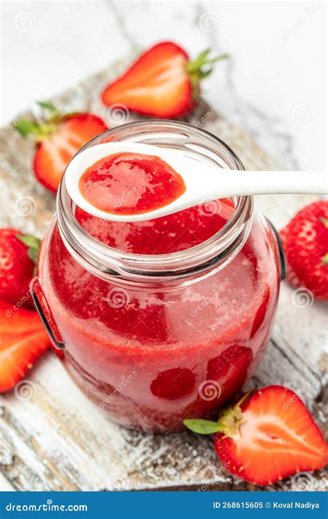 Primer plano de un frasco de mermelada de fresa con fresas frescas alrededor.
