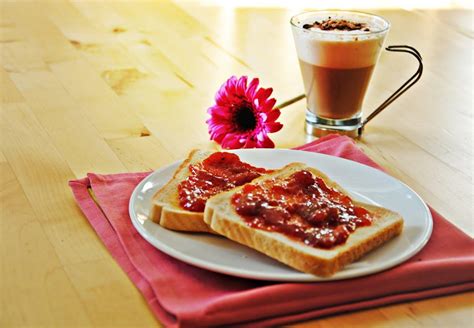 Fotografía de una mesa de desayuno familiar con tostadas, mermeladas y una taza de café con leche.