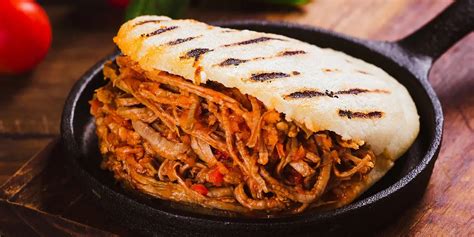 Fotografía gastronómica de una arepa abierta y rellena con carne desmechada, aguacate y queso.