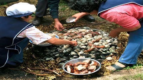 Fotografía detallada de un curanto en hoyo tradicional siendo preparado con hojas de nalca