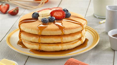 Foto de panqueques dorados apilados, decorados con frutas frescas y jarabe