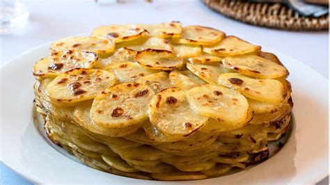 Fotografía profesional de un milhojas de papa y verduras recién salido del horno, mostrando las capas finas y una superficie dorada y gratinada