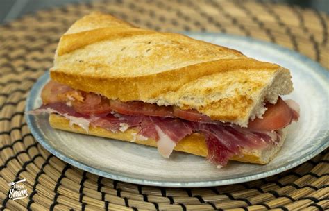 Esquema de los pasos para preparar un bocadillo tradicional: corte del pan, restregado del tomate, aderezo con aceite y colocación del jamón