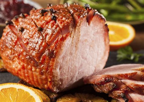 jamón glaseado entero sobre una tabla, listo para ser cortado, con guarniciones de puré de papas y col rizada al fondo
