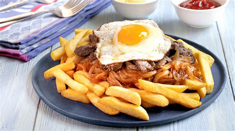 Fotografía gastronómica de una chorrillana tradicional servida con papas fritas, carne y huevos.