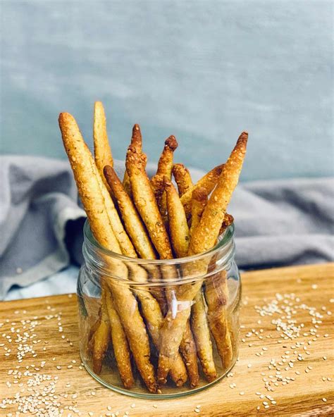 Grisines caseros de harina de garbanzo recién horneados, espolvoreados con semillas de sésamo, sobre papel de horno.