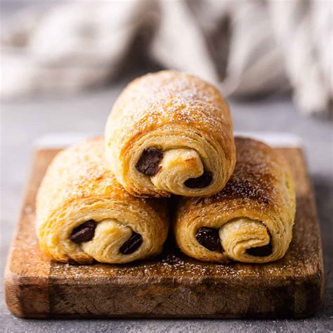 Fotografía profesional de un pain au chocolat recién horneado con capas de hojaldre visibles y relleno de chocolate.