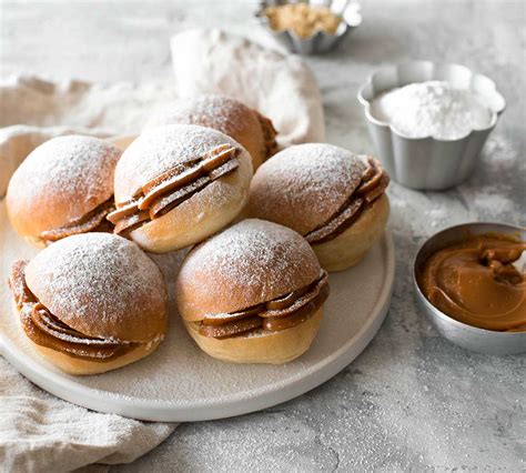 Fotografía profesional de berlines horneados espolvoreados con azúcar flor y rellenos de manjar.