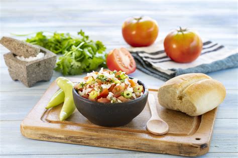 Fotografía de un bol con pebre fresco acompañado de pan amasado y un pocillo de ají verde.