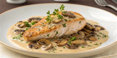 Plato gourmet de pechuga de pollo bañada en salsa de crema de champiñones y queso, decorado con hierbas frescas