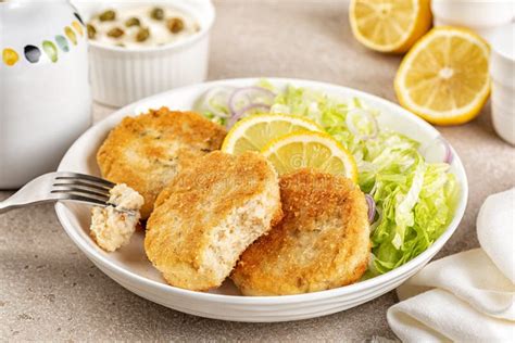Presentación de hamburguesas de medallones de pescado servidas con ensalada fresca y salsa tártara.