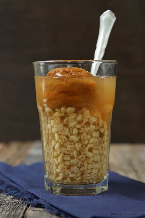 Fotografía de un vaso alto con mote con huesillos servido, mostrando la capa de trigo en el fondo, los duraznos rehidratados y el jugo color caramelo
