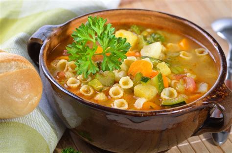 Un plato humeante de sopa menestrón, lleno de verduras y pasta, servido en un cuenco rústico.