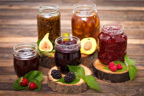Fotografía de un surtido de mermeladas artesanales en frascos, con frutas frescas de fondo