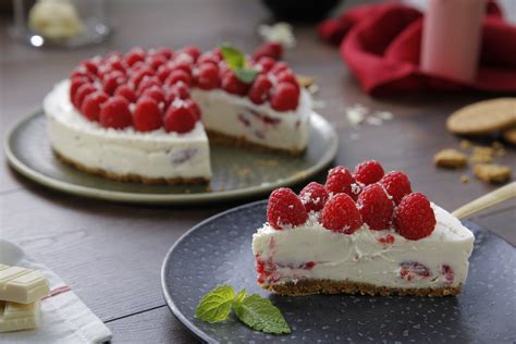 Fotografía de una tarta de chocolate blanco con frambuesas sobre un elegante stand de madera y mármol