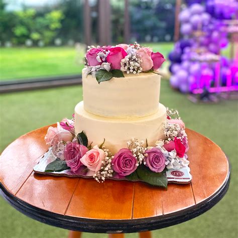 Diseñador: Una mesa de postres elegante con un pastel decorado con flores naturales, rodeado de arreglos florales frescos y detalles dorados.