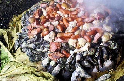 Fotografía de un curanto al hoyo siendo destapado, con el vapor escapando y mostrando las capas de ingredientes.