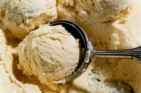 Fotografía profesional de una bola de helado de vainilla con una capa crujiente de chocolate y trozos de frutos secos o galletas.