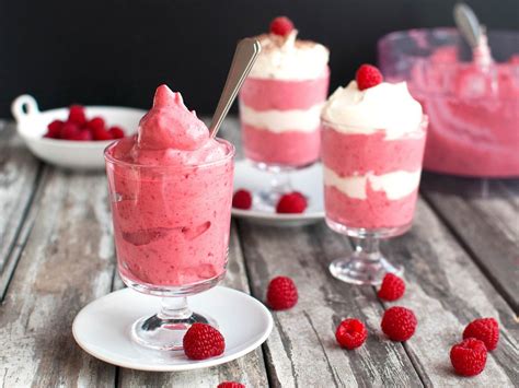 Foto de una crema o mousse de frambuesa y nata servida en copas, decorada con frambuesas frescas y hojas de menta.