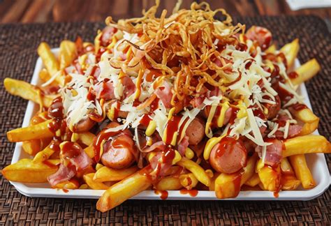 Plato de salchipapa casera servida con abundante salsa de queso derretido, salchichas doradas y papas fritas crujientes.