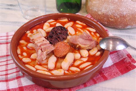 Plato de fabada asturiana servido en una cazuela de barro con el compango al lado